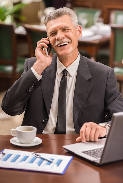 Uomo d'affari maturo elegante che si siede al tavolo in caffè.