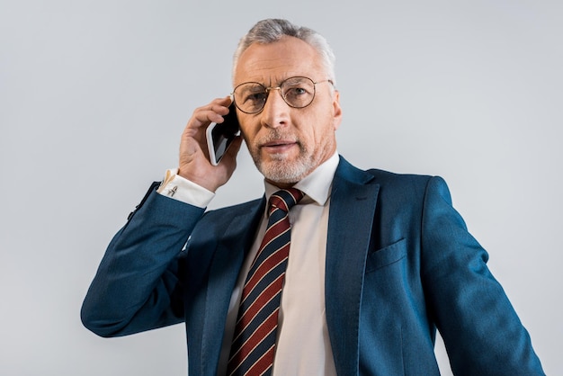 Uomo d'affari maturo in giacca e cravatta che parla su smartphone isolato su grigio
