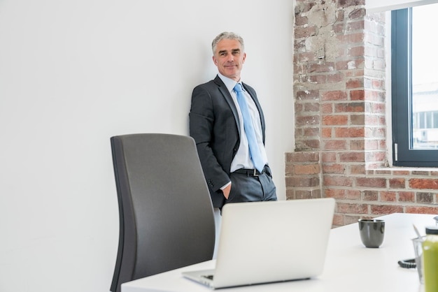 Uomo d'affari maturo in piedi in ufficio, guardando fiducioso