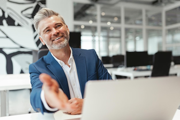 Uomo d'affari maturo sorridente che lavora con il computer portatile mentre è seduto nel coworking moderno