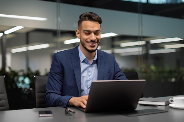 Uomo d'affari mediorientale sorridente che digita sul computer in ufficio