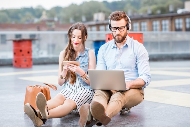 Uomo d'affari moderno e donna d'affari che lavora con laptop e telefono seduto sul terreno dell'eliporto. Concetto di affari di stile di vita