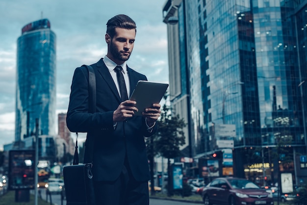 Uomo d'affari moderno. Immagine notturna di un giovane fiducioso in completo che tiene in mano un tablet digitale