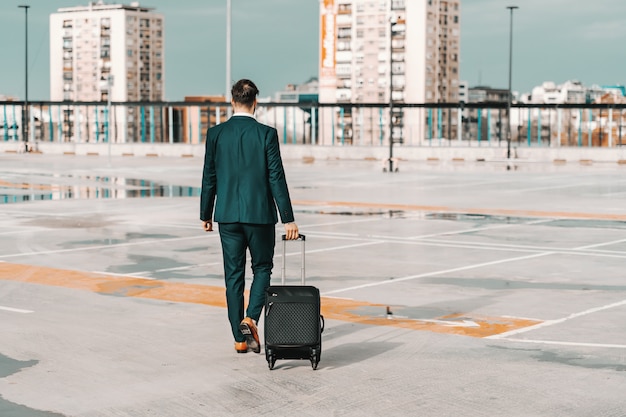 Uomo d'affari nei bagagli della tenuta di usura convenzionale e camminare sul parcheggio. Concetto di viaggio d'affari.