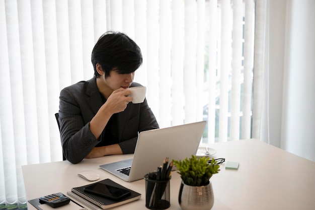 Uomo d'affari pacifico che beve caffè e legge i dati aziendali sul computer portatile