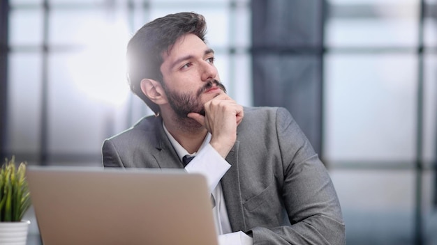 Uomo d'affari pensieroso che si siede alla tavola con il computer portatile