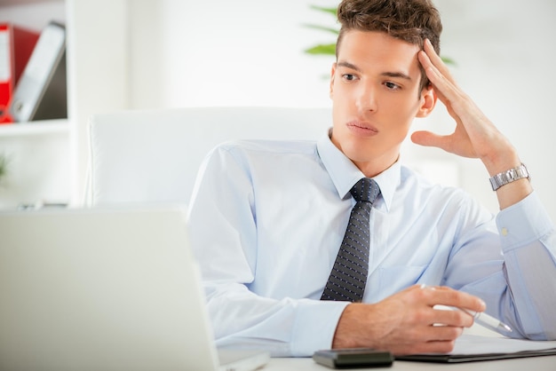 Uomo d'affari pensieroso seduto con il computer portatile in ufficio.