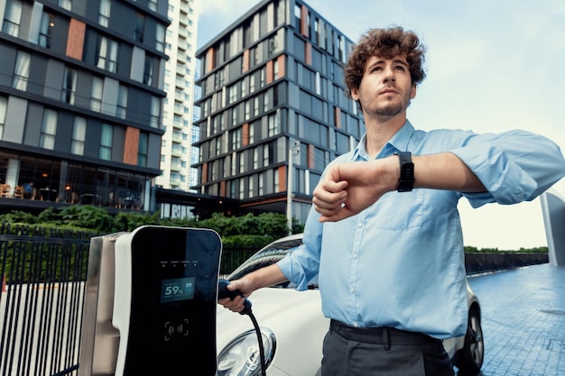 Uomo d'affari progressista con smartwatch presso la stazione di ricarica pubblica per auto EV