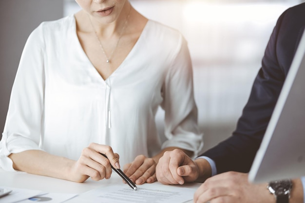 Uomo d'affari sconosciuto e donna che discutono del contratto in ufficio soleggiato, primo piano. Uomini d'affari o avvocati che lavorano insieme alla riunione.