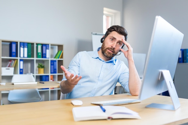 Uomo d'affari sconvolto con auricolare che lavora in ufficio con il computer