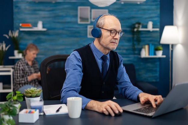 Uomo d'affari senior che ascolta musica che indossa le cuffie che lavorano sul laptop