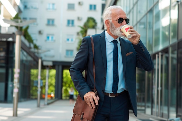 Uomo d'affari senior che cammina e beve caffè