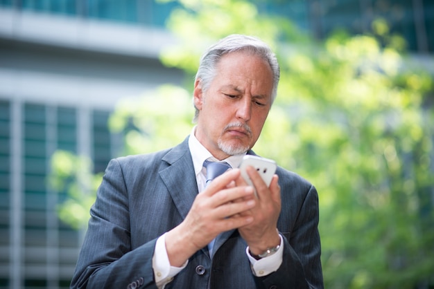 Uomo d'affari senior che utilizza il suo smartphone all'aperto