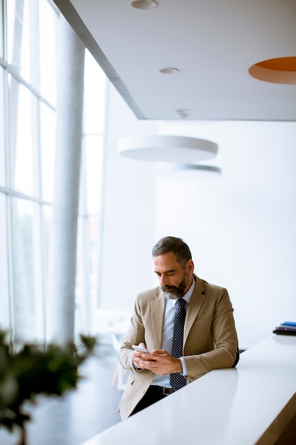 Uomo d'affari senior che utilizza telefono cellulare nell'ufficio moderno