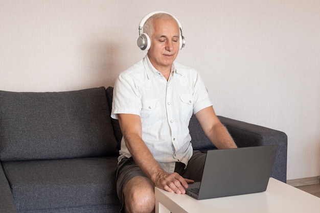 Uomo d'affari senior dell'uomo che lavora al computer a casa che indossa le cuffie