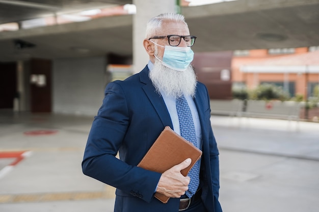 Uomo d'affari senior hipster che indossa una maschera di sicurezza alla stazione degli autobus - Focus on face