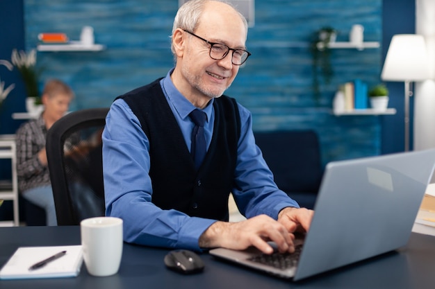 Uomo d'affari senior intelligente che lavora al computer portatile che indossa una cravatta e occhiali and