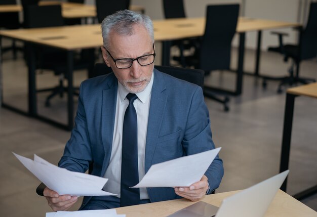 Uomo d'affari senior pensieroso che legge il rapporto finanziario