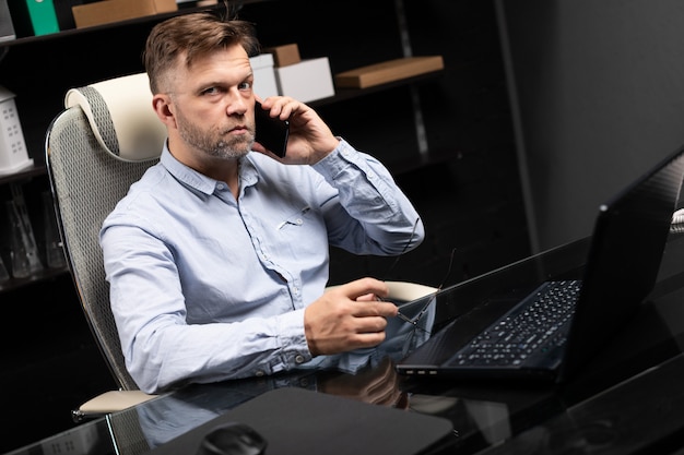 Uomo d&#39;affari serio che lavora ad un computer portatile e che parla su un telefono cellulare