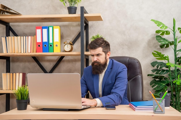 Uomo d'affari serio che lavora al computer portatile al lavoro della scrivania