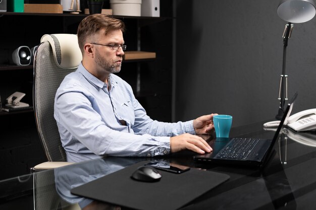 Uomo d'affari serio che lavora al computer portatile e che beve caffè