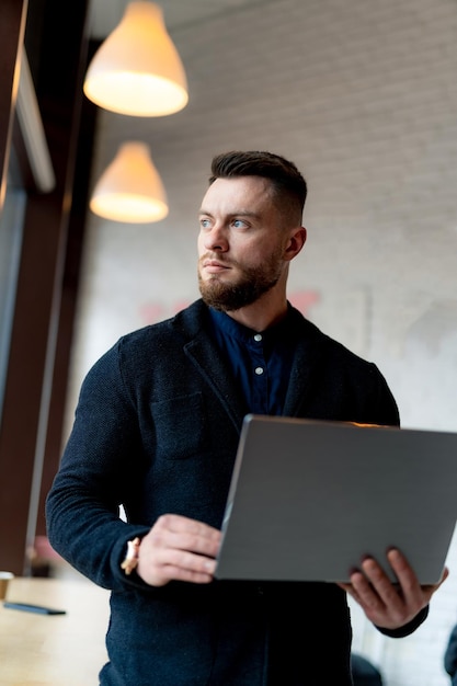 Uomo d'affari serio che lavora nella caffetteria mentre tiene il suo laptop e guarda la finestra Uomo che lavora sul concetto di distanza