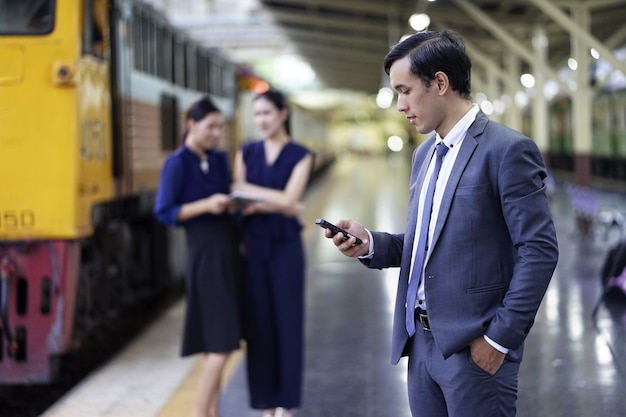 Uomo d&#39;affari serio che manda un sms sul cellulare mentre due suoi colleghi che parlano vicenda a subw