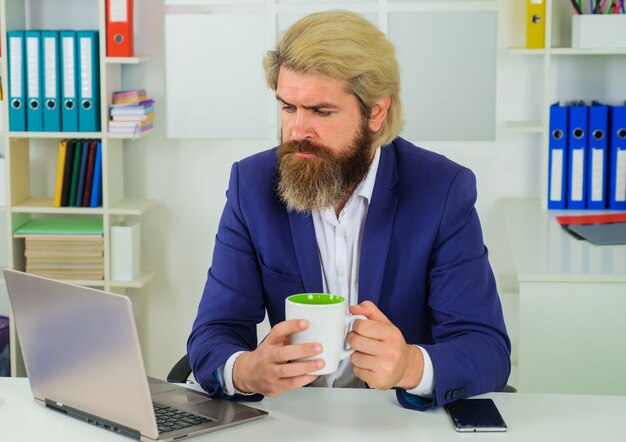 Uomo d'affari serio in vestito che beve caffè. Uomo d'affari in ufficio. Caffè mattutino al lavoro.