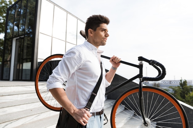 Uomo d'affari serio vestito in camicia che trasporta una bicicletta