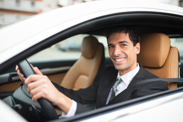 Uomo d'affari sorridente alla guida della sua nuova automobile bianca