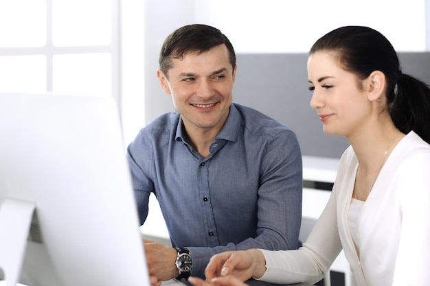 Uomo d'affari sorridente allegro e donna che lavora con il computer in ufficio moderno. Colpo alla testa durante una riunione o sul posto di lavoro. Concetto di lavoro di squadra, partnership e business.