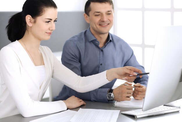 Uomo d'affari sorridente allegro e donna che lavora con il computer in ufficio moderno. Colpo alla testa durante una riunione o sul posto di lavoro. Concetto di lavoro di squadra, partnership e business.