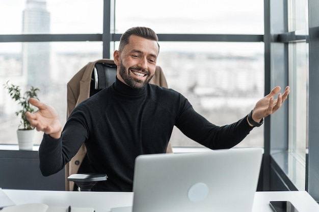 Uomo d'affari sorridente che comunica tramite videoconferenza utilizzando il laptop in ufficio