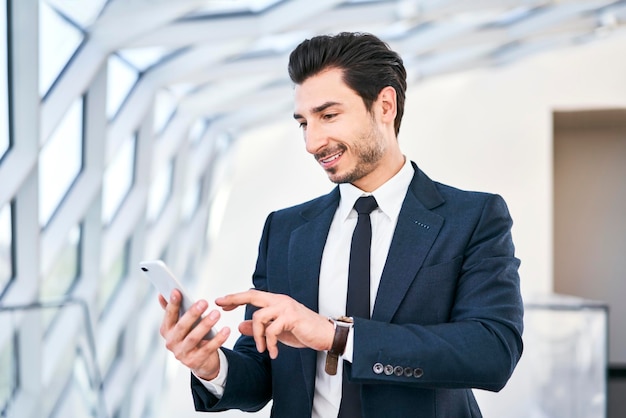 Uomo d'affari sorridente che esamina il telefono cellulare