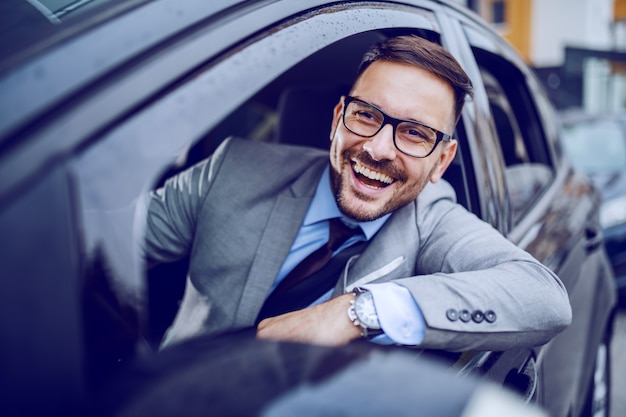 Uomo d'affari sorridente che guarda la finestra della depressione mentre conducendo la sua automobile costosa. Concetto di viaggio d'affari.