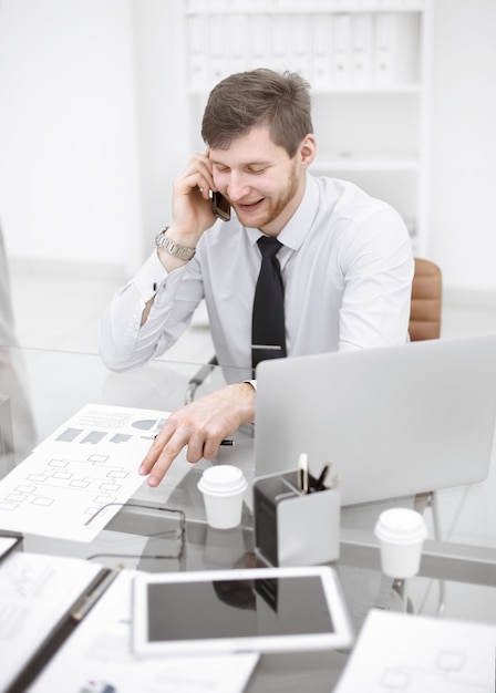 Uomo d'affari sorridente che parla al telefono seduto alla sua scrivania