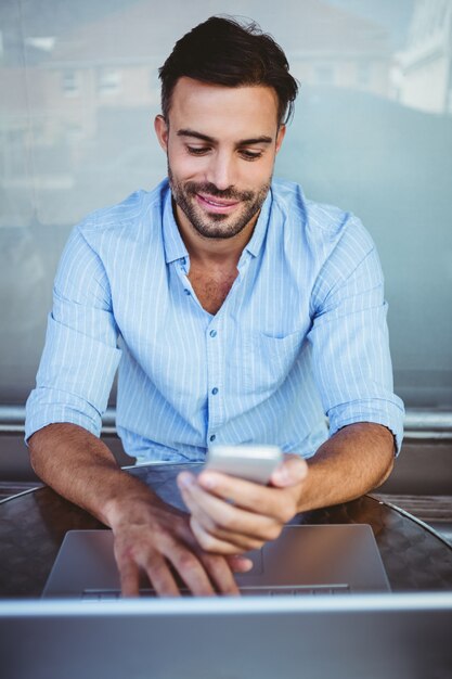 Uomo d&#39;affari sorridente che utilizza telefono mentre lavorando al computer portatile