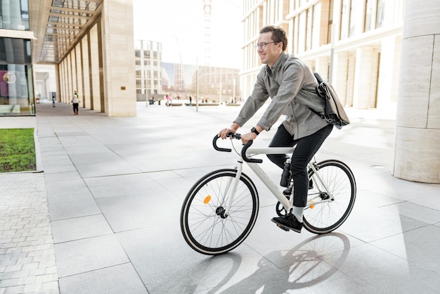 Uomo d'affari sorridente che va in bicicletta in un paesaggio urbano moderno che promuove i viaggi sostenibili