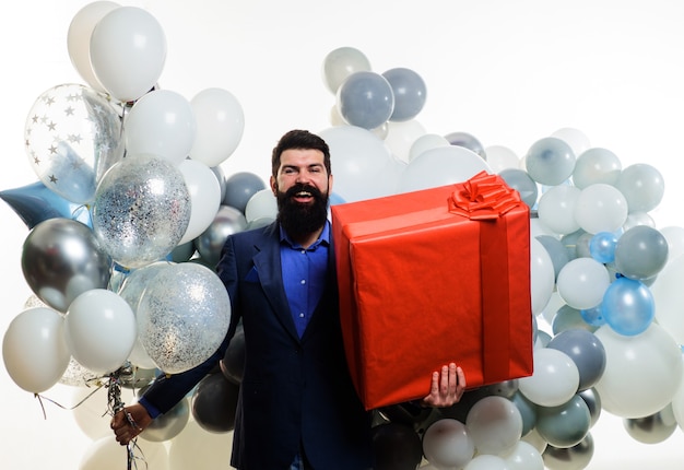 Uomo d'affari sorridente con palloncini di elio e grande scatola regalo. Uomo barbuto con regalo. Compleanno, vacanze, celebrazione.