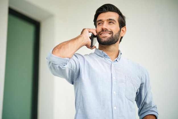 Uomo d'affari sorridente con smart phone Dirigente bello che guarda lontano mentre si trova contro il muro Indossa abiti casual intelligenti