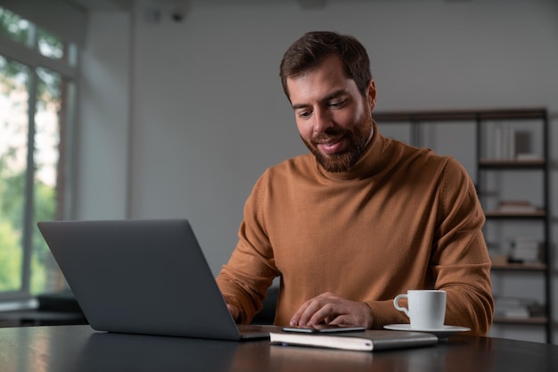 Uomo d'affari sorridente in abbigliamento casual che lavora al computer portatile in ufficio