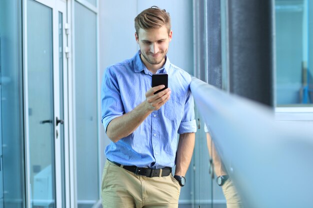 Uomo d'affari sorridente in piedi e utilizzando il telefono cellulare in ufficio.