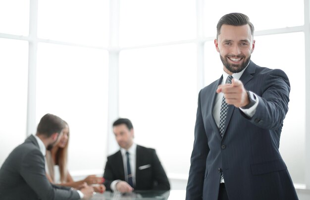 Uomo d'affari sorridente in piedi in ufficio e indicando youphoto con spazio di copia