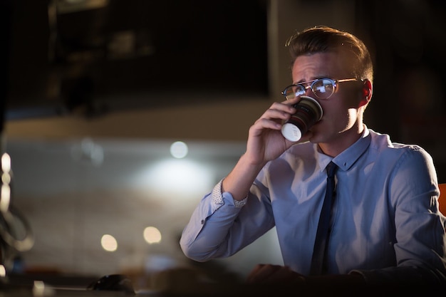 Uomo d'affari stanco che lavora fino a tardi facendo gli straordinari in ufficio di notte a bere caffè per andare avanti.