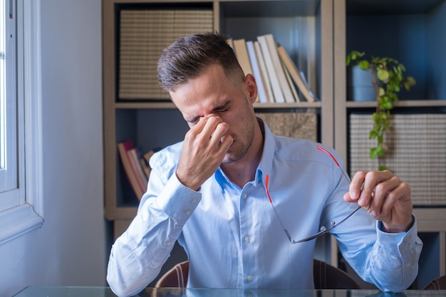 Uomo d'affari stressato malsano che si toglie gli occhiali, si sfrega le palpebre, soffre di sindrome degli occhi asciutti a causa del lungo superlavoro del computer, massaggia il ponte della testa per alleviare il dolore in ufficio a casa.