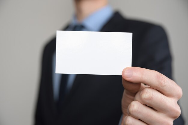 Uomo d'affari, stretta della mano dell'uomo di affari che mostra biglietto da visita - immagine ravvicinata su sfondo grigio. Mostra un foglio di carta bianco. Biglietto da visita cartaceo.