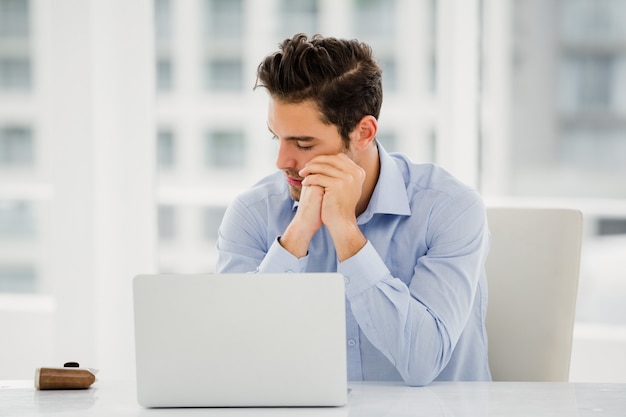 Uomo d'affari teso che si siede alla tavola con il computer portatile