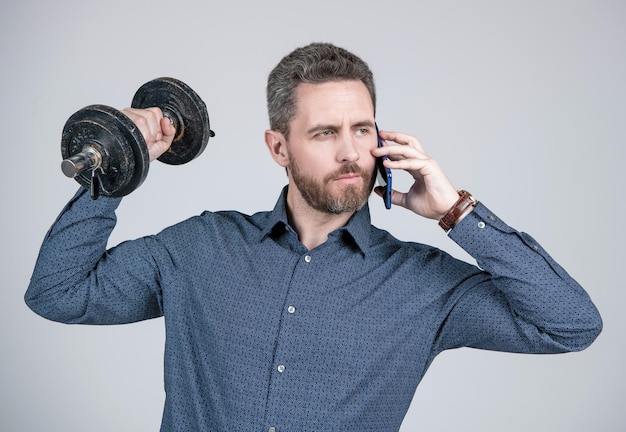 Uomo d'affari uomo barbuto forte che si allena con il bilanciere e parla sullo smartphone, ciao.