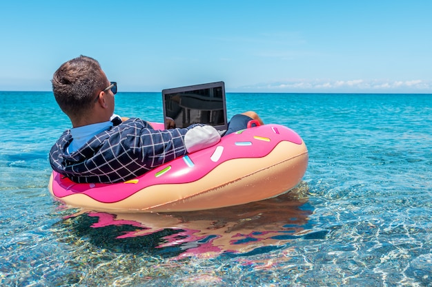 Uomo d'affari utilizzando il computer portatile su una ciambella gonfiabile in mare