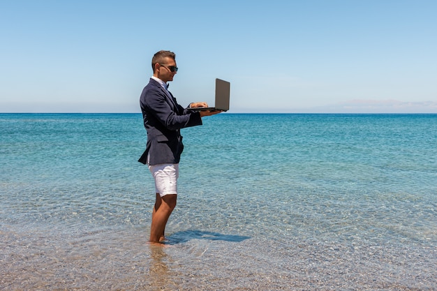 Uomo d'affari utilizzando il computer portatile sulla spiaggia tropicale